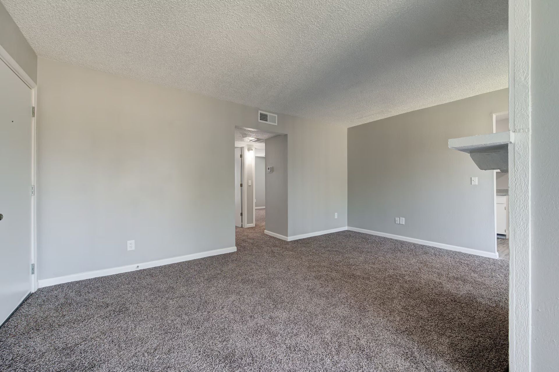 Empty apartment living room with gray walls, carpet, and a hallway.