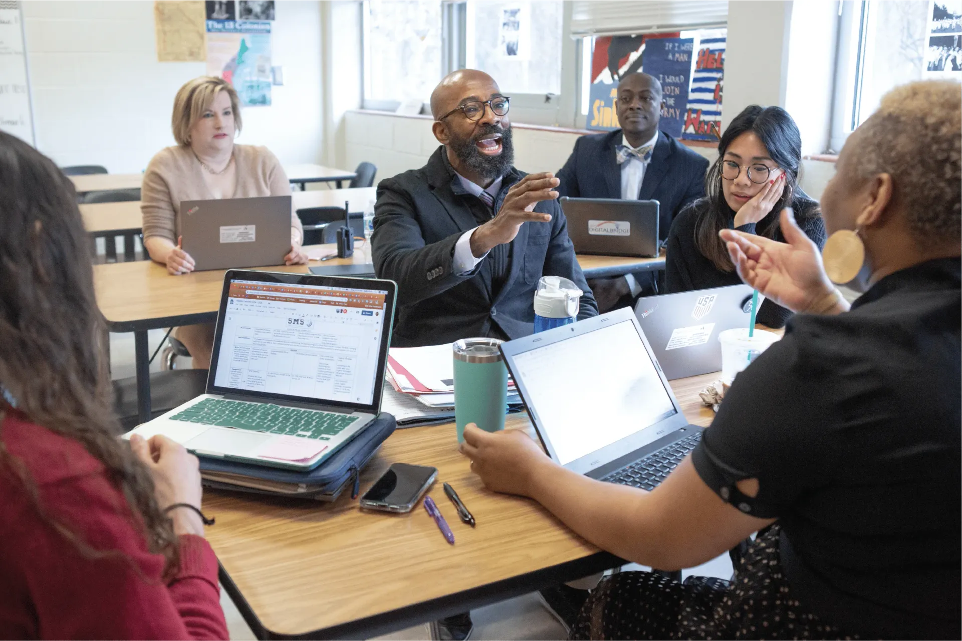 A group of people are sitting around a table with laptops.