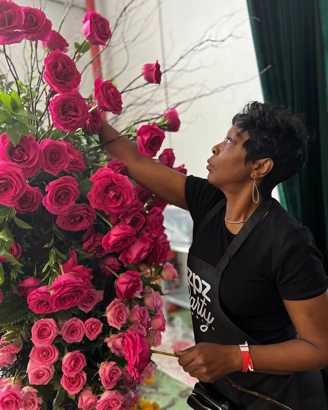 A woman in a black apron is arranging pink roses