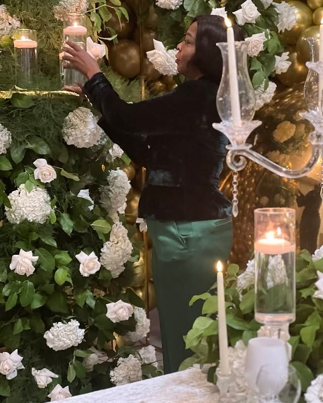 A woman is standing in front of a wall of flowers and candles.