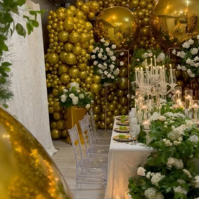 A long table with plates and candles in front of a wall of gold balloons.