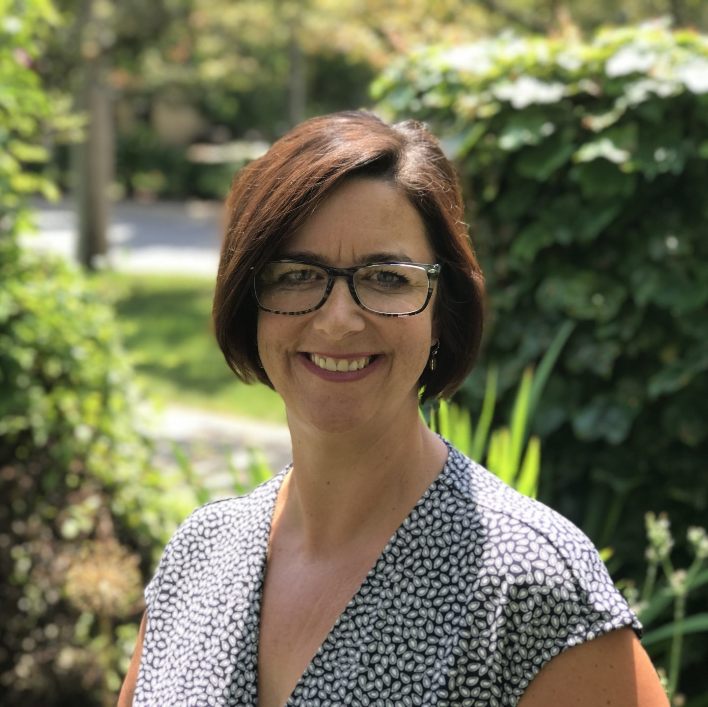 A woman wearing glasses and a polka dot shirt is smiling for the camera.