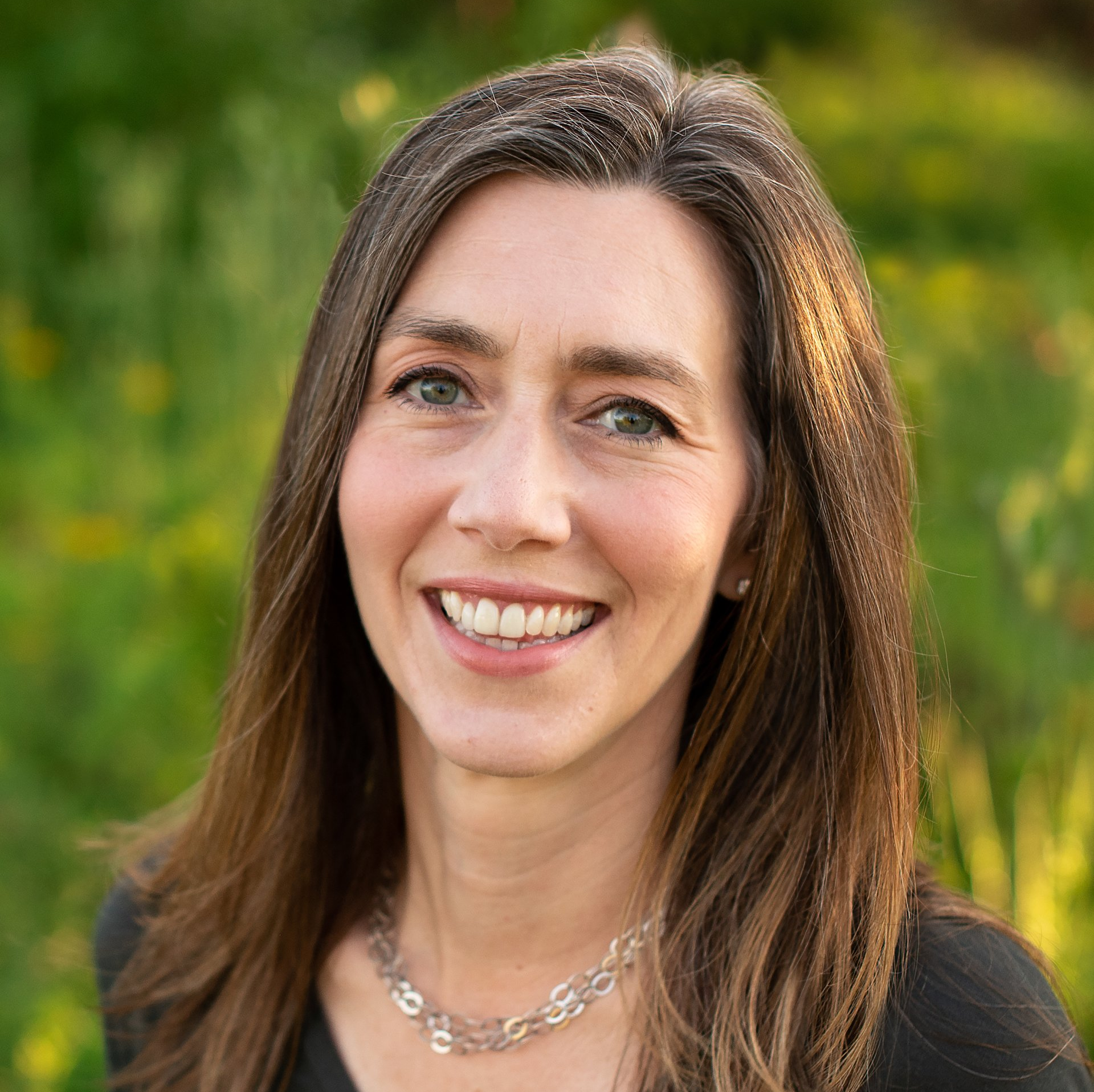 A woman wearing a necklace and a black shirt is smiling for the camera.