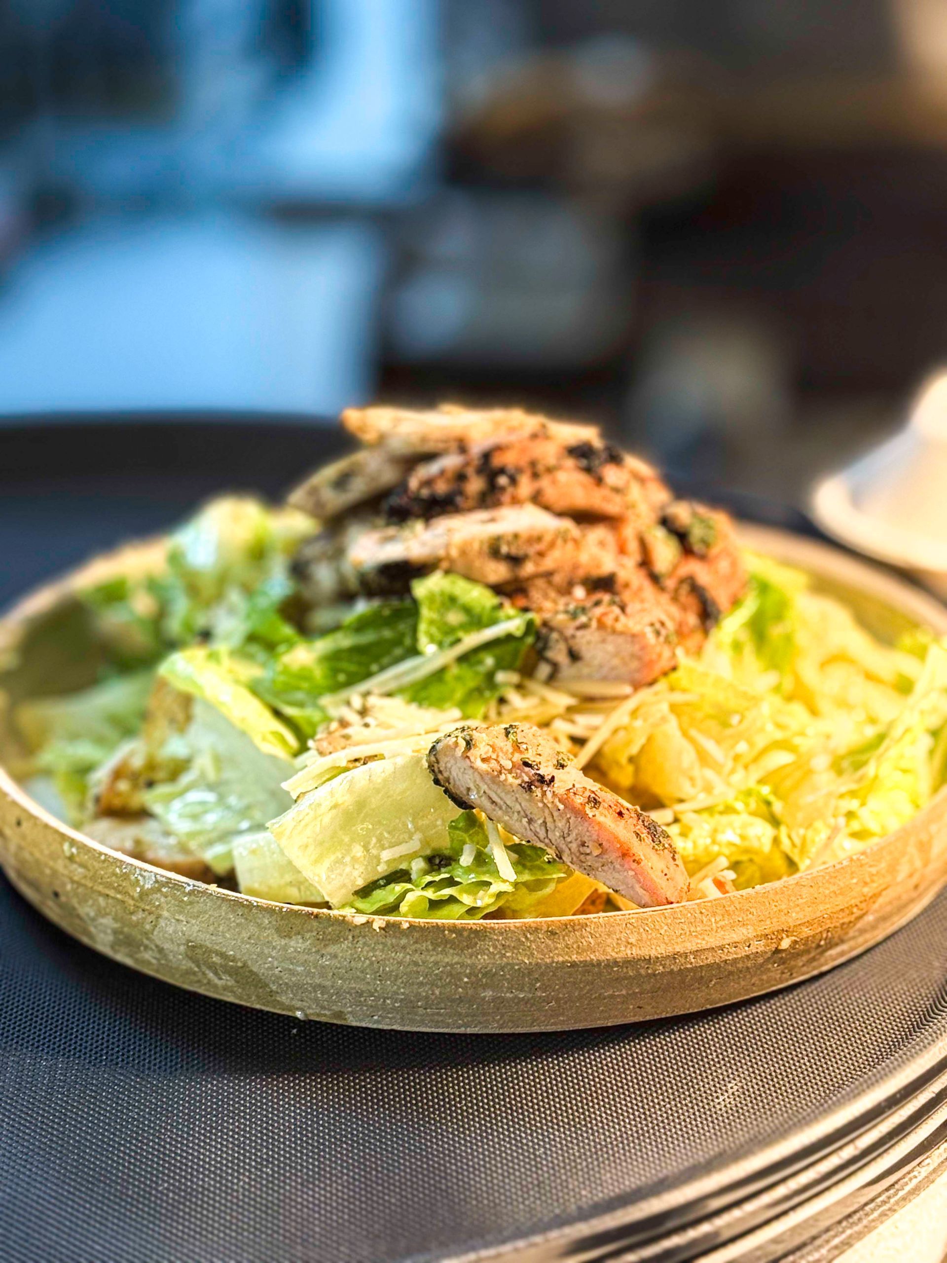 Chicken Caesar salad in a rustic bowl on a black tray.