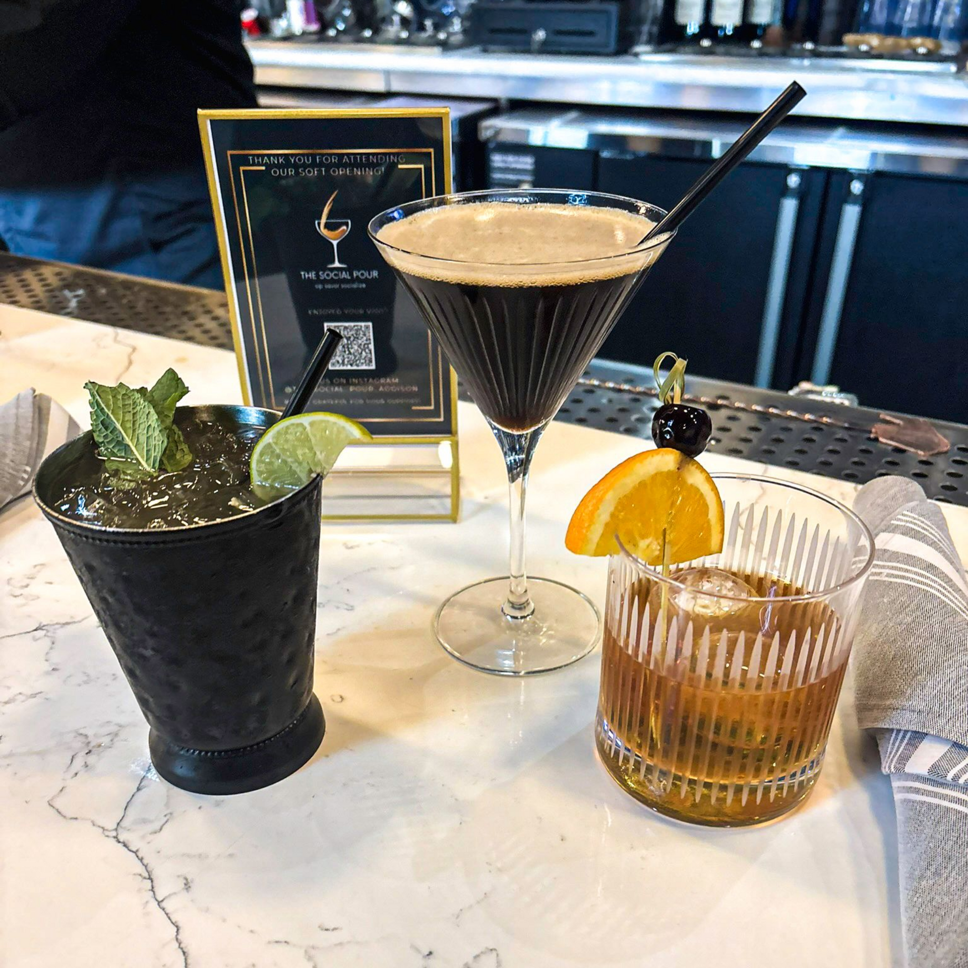 Three cocktails on a marble bar: mint julep, espresso martini, and old fashioned.