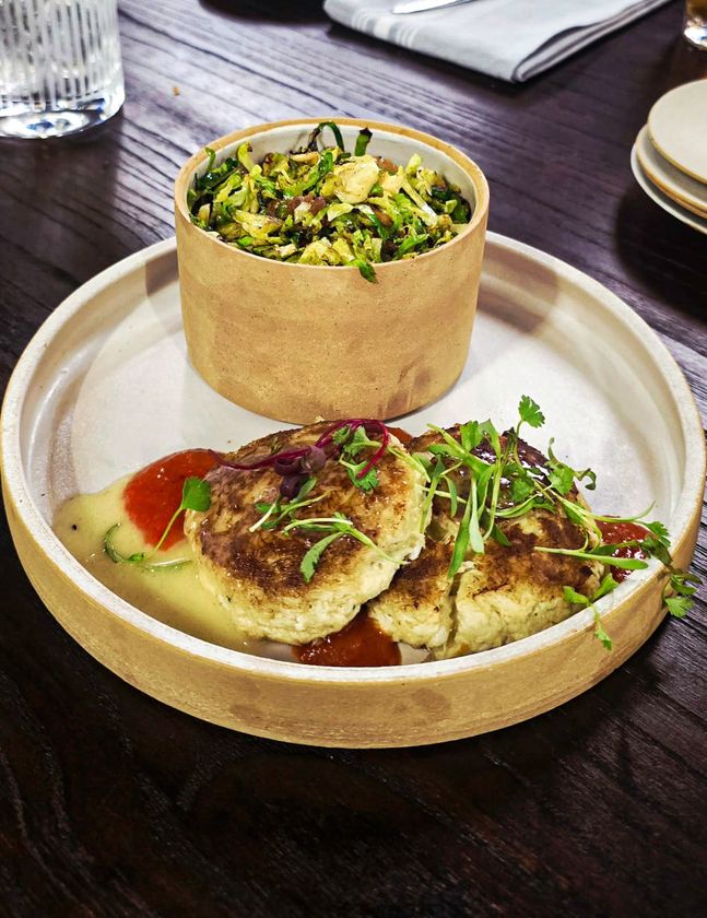 Plate with two crab cakes, a side of slaw in a round container, and sauces.