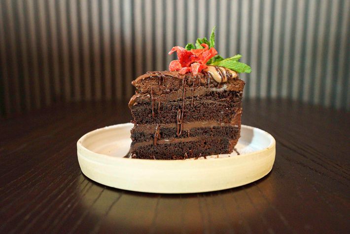 Chocolate cake slice with chocolate mousse filling, topped with a dark glaze and berry pieces on a white plate.