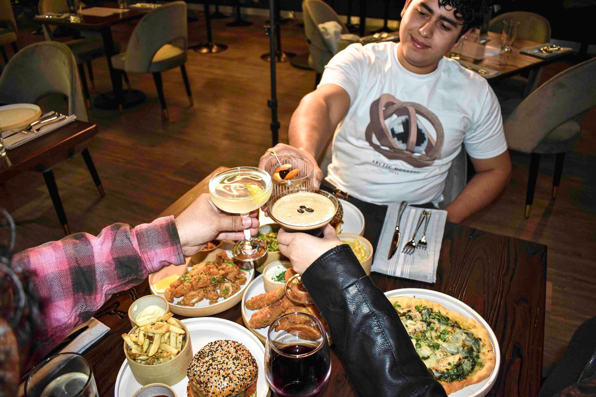 People clink glasses at a restaurant table with food.