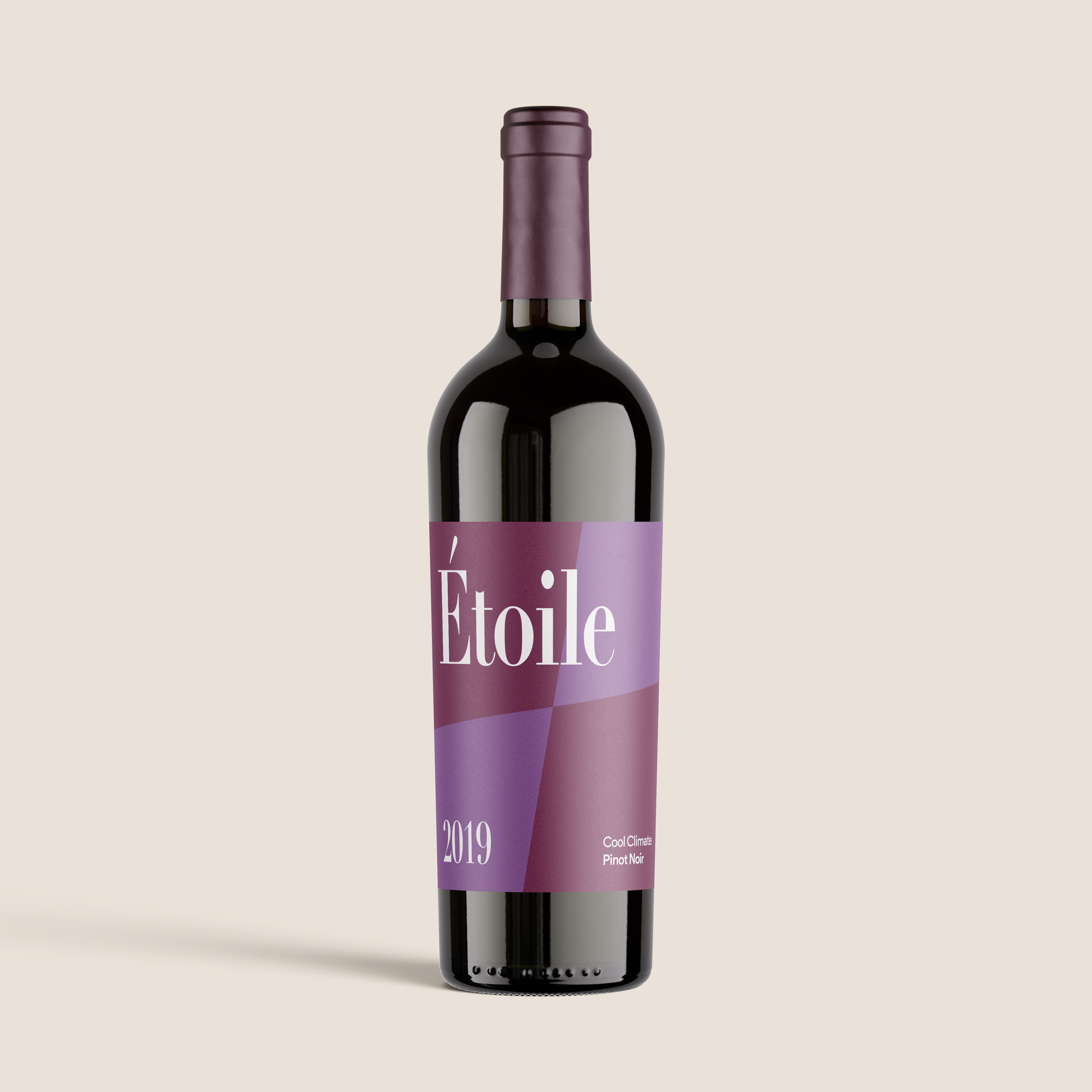 Bottle of Étoile wine, purple label, black glass, angled against a beige background.