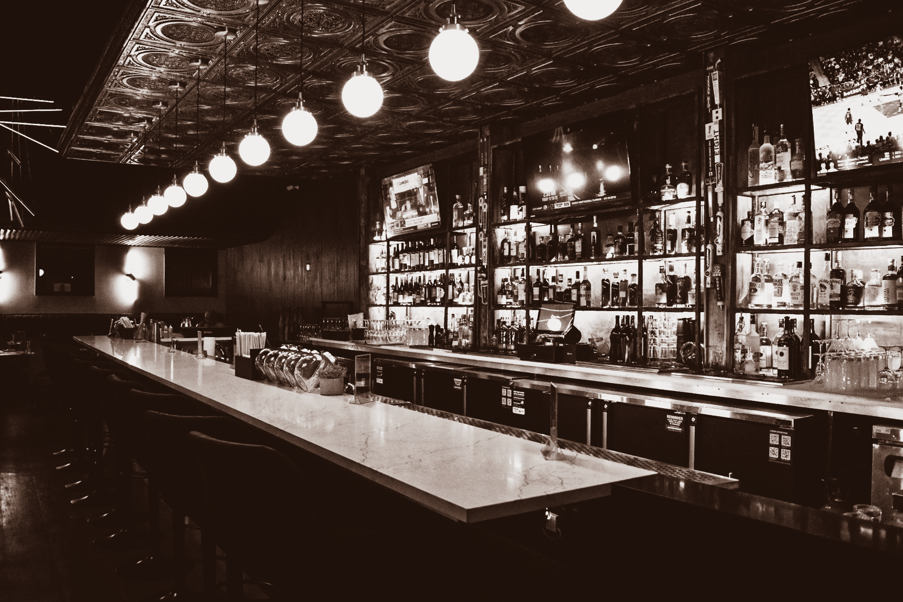 Long, illuminated bar with many bottles, in an interior with dimmed lights.