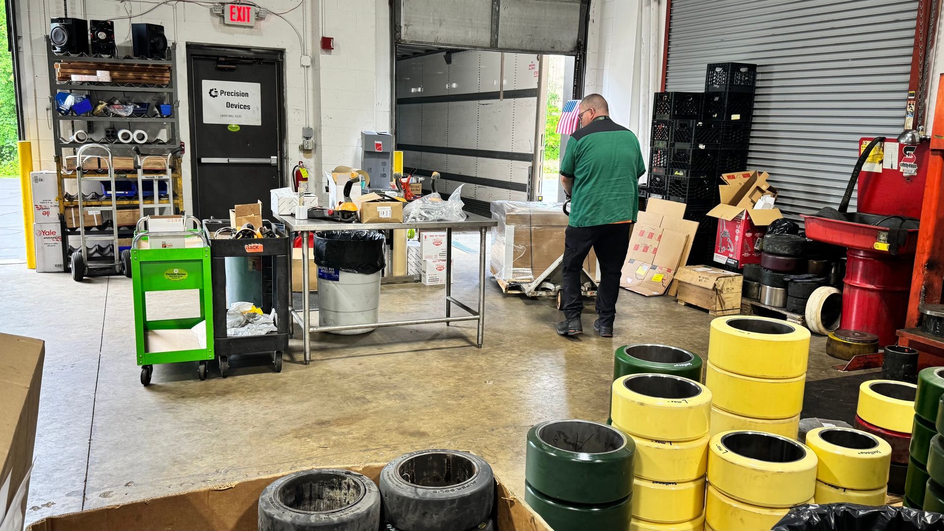 A man in a green jacket is standing in a warehouse surrounded by stacks of tires.