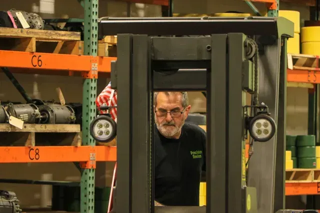A man in a green jacket is standing in a warehouse surrounded by stacks of tires.