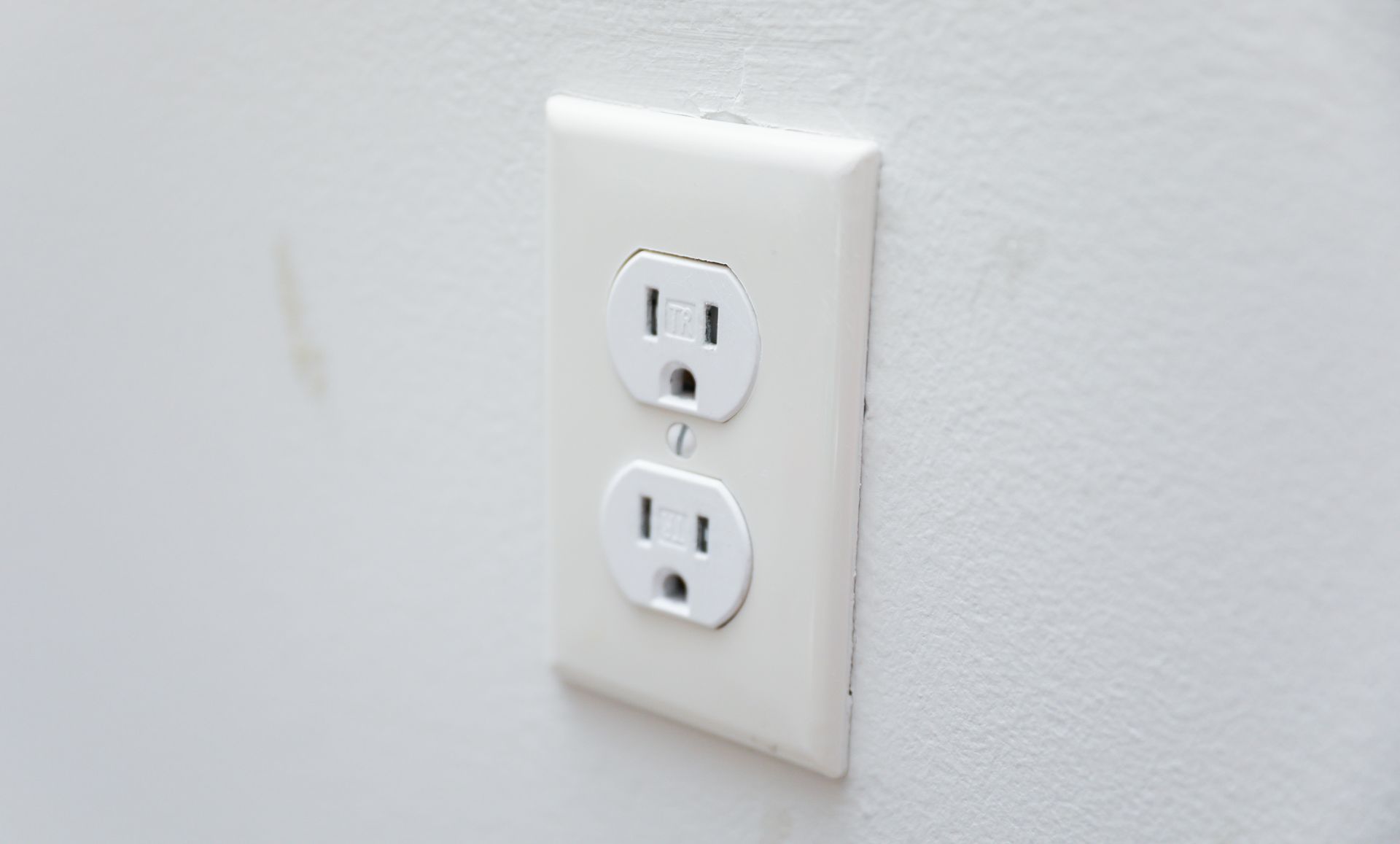 A close up of a white electrical outlet on a white wall.