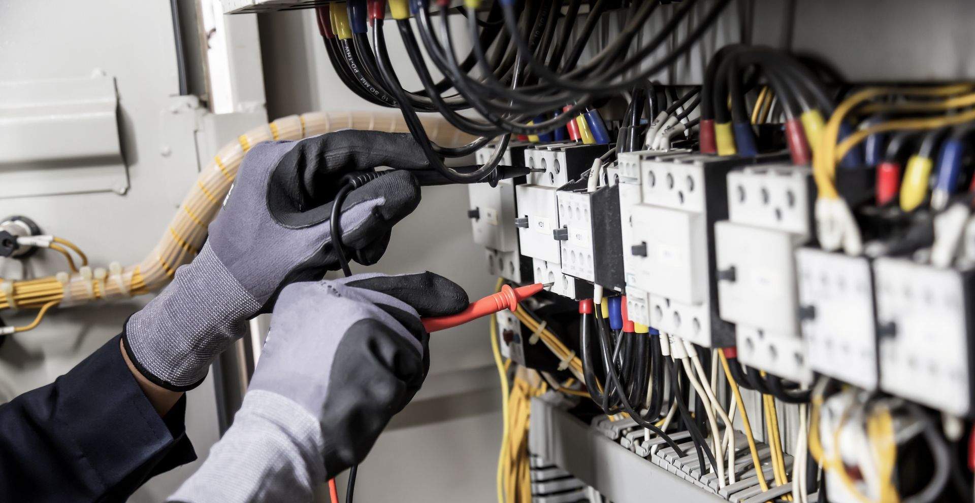 An electrician is working on an electrical panel with a multimeter.