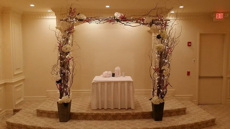 Decorated archway framing a small white table in a beige event hall, with an exit sign nearby