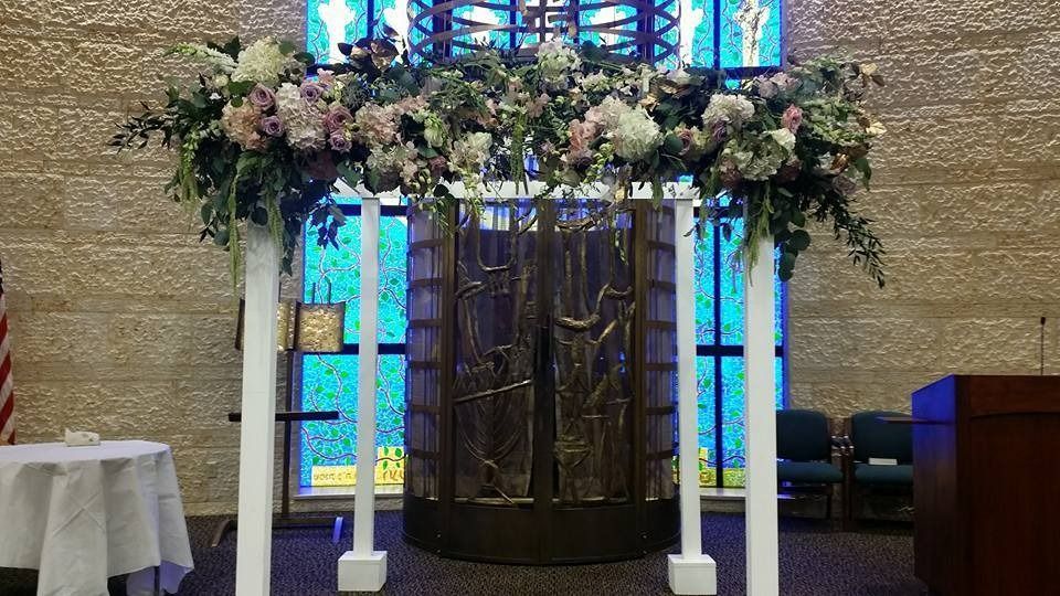 Floral arch over a church baptismal font with stained glass windows behind it