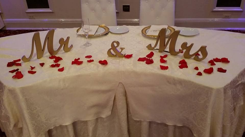 Gold “Mr & Mrs” signs with red rose petals on a decorated table