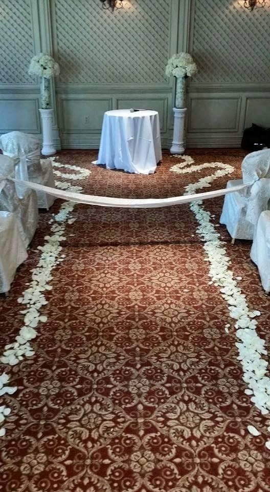 Decorated aisle with patterned red carpet, white drapes, and a small table at the end in a ceremony room