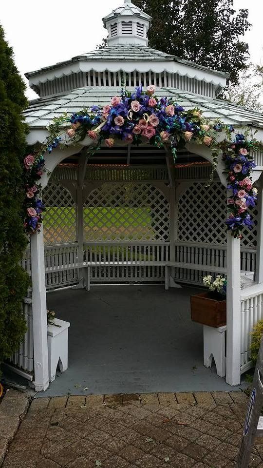 White garden gazebo with pink and purple flowers around the entrance and lattice walls.