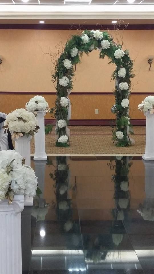 Floral wedding arch with white chairs in a banquet hall, reflected on a glossy floor