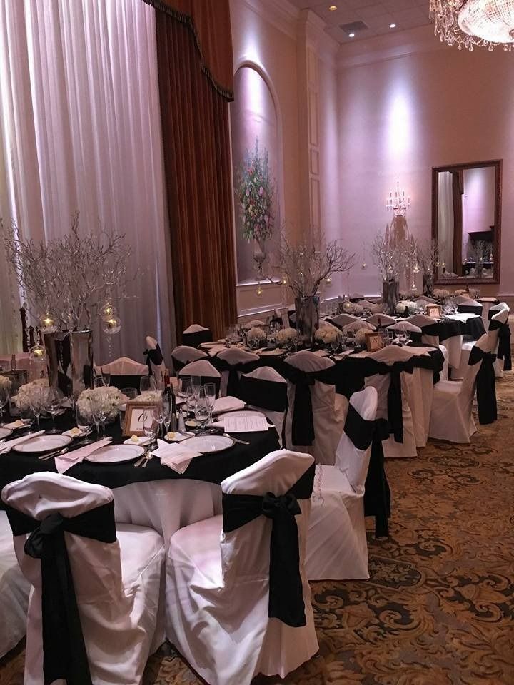 Elegant banquet hall with round tables, black-and-white chair covers, and tall white drapes.