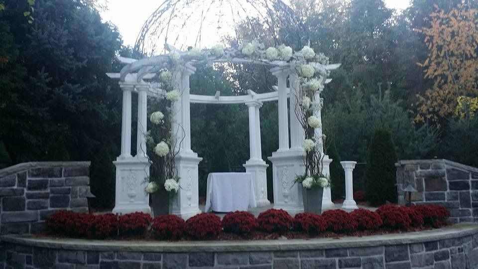 White floral wedding arch with draped fabric and candles in a stone garden courtyard