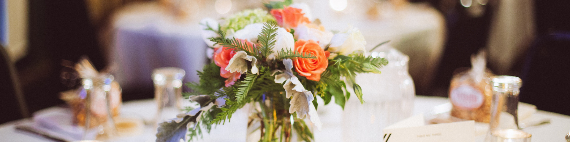 Elegant banquet table centerpiece with white flowers, greenery, and orange roses on a white tablecloth