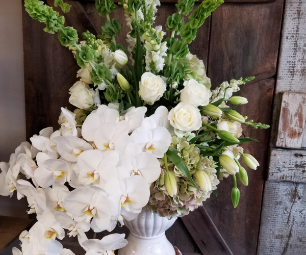 White orchids and roses in a vase against a rustic wooden backdrop