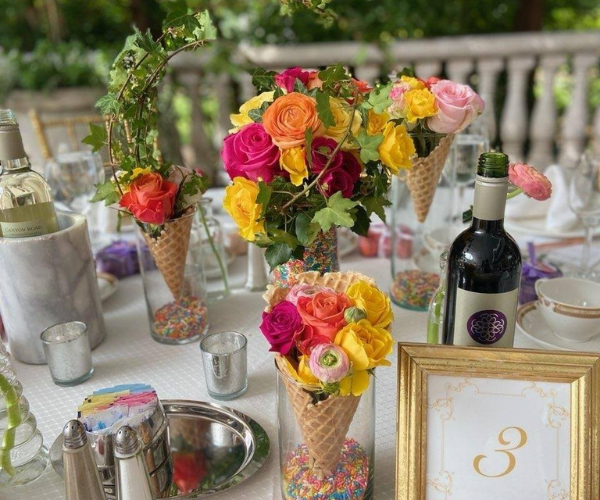 Colorful floral arrangements in waffle cones on a decorated table with champagne and a gold-framed number 3 sign