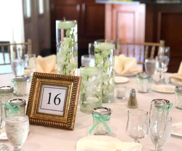 Elegant banquet table with table number 16, white linens, glassware, and pale green floral decor