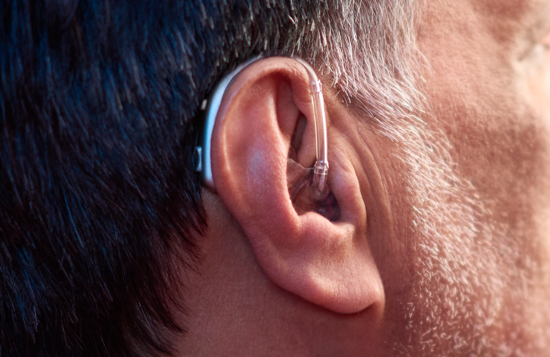 Close-up of ear with hearing aid behind the ear, gray hair.