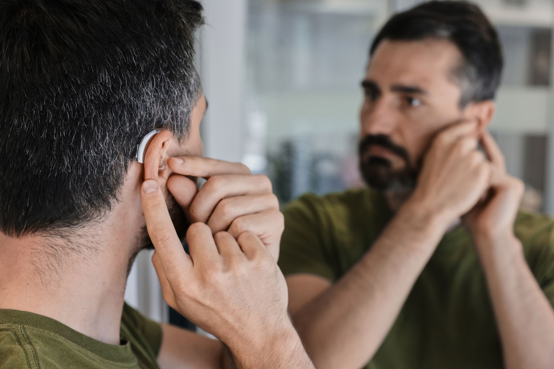 Man adjusting his hearing aid while looking in a mirror.
