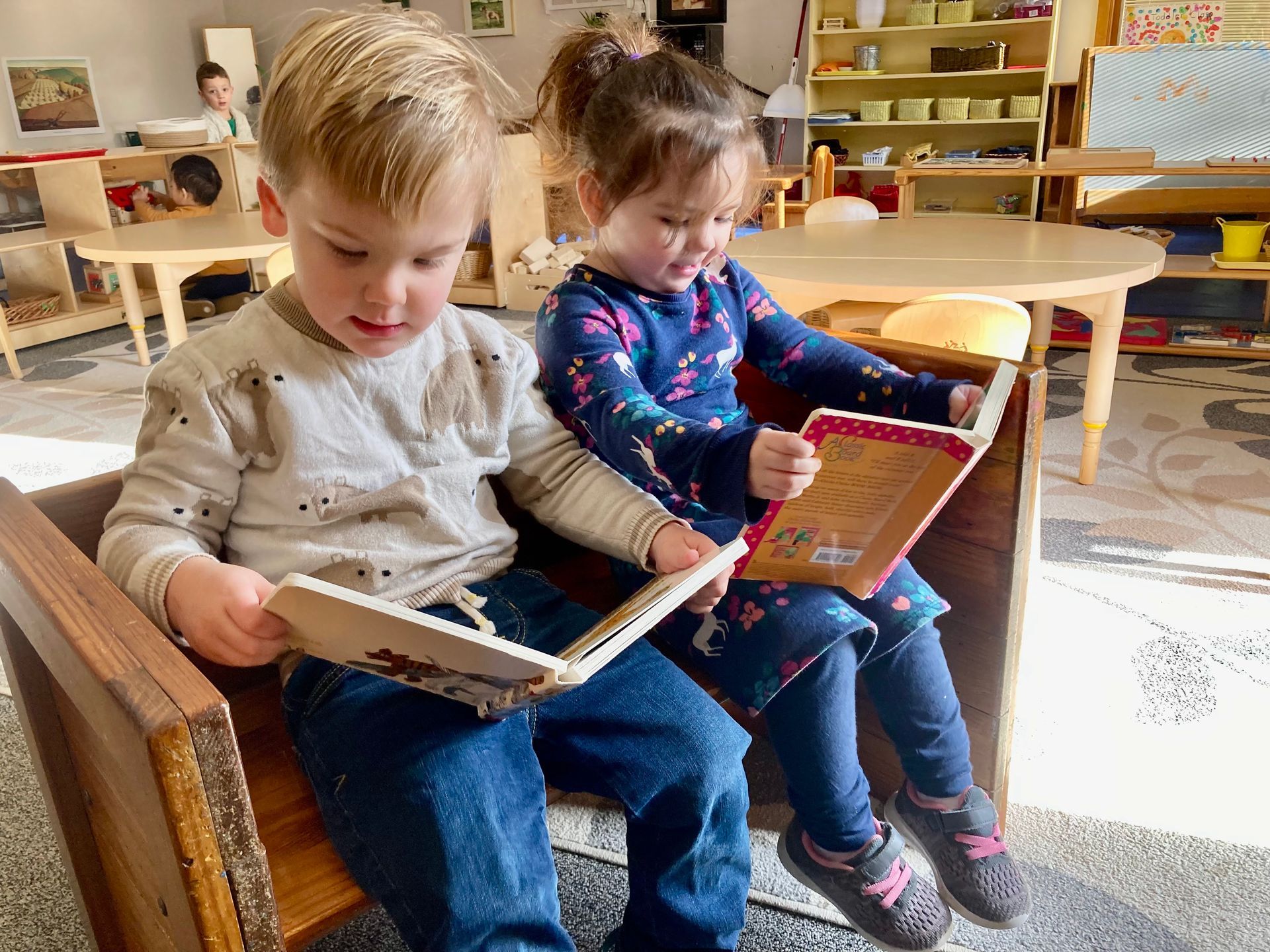 Montessori children are sitting in chairs reading books.