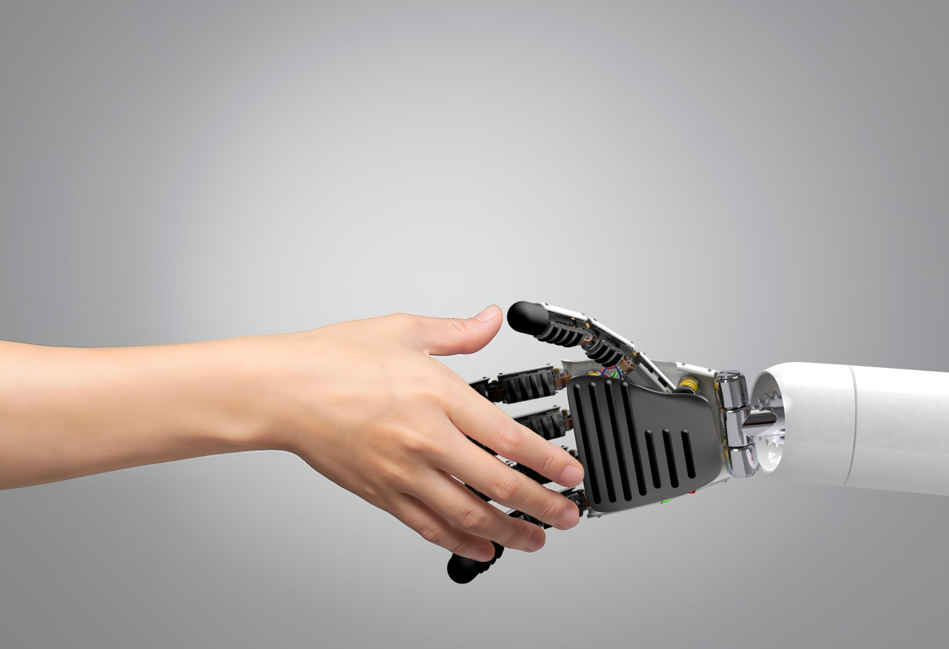 Human hand shaking a robotic hand, grey background.