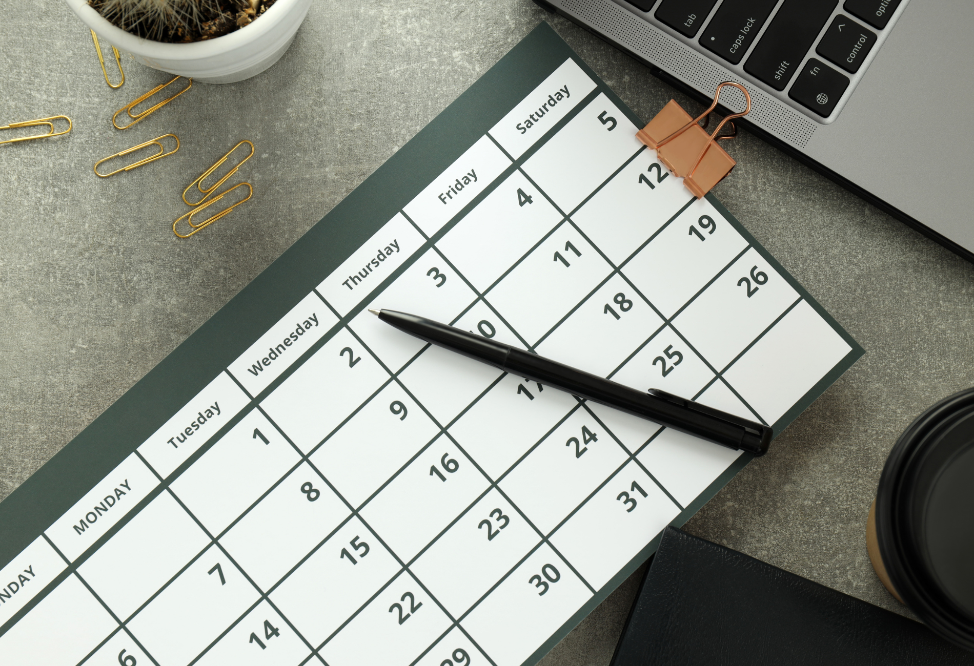 A calendar with a pen, laptop, and supplies on a gray surface.