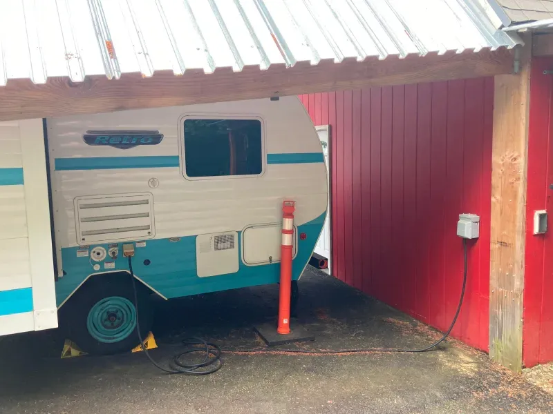 A blue and white trailer is parked under a roof next to a red wall.
