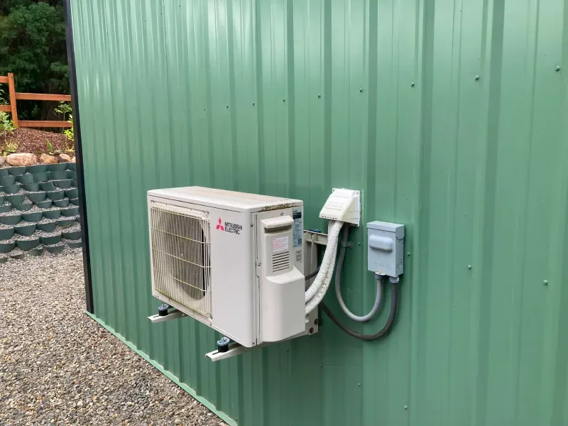 A white air conditioner is mounted on the side of a green building.