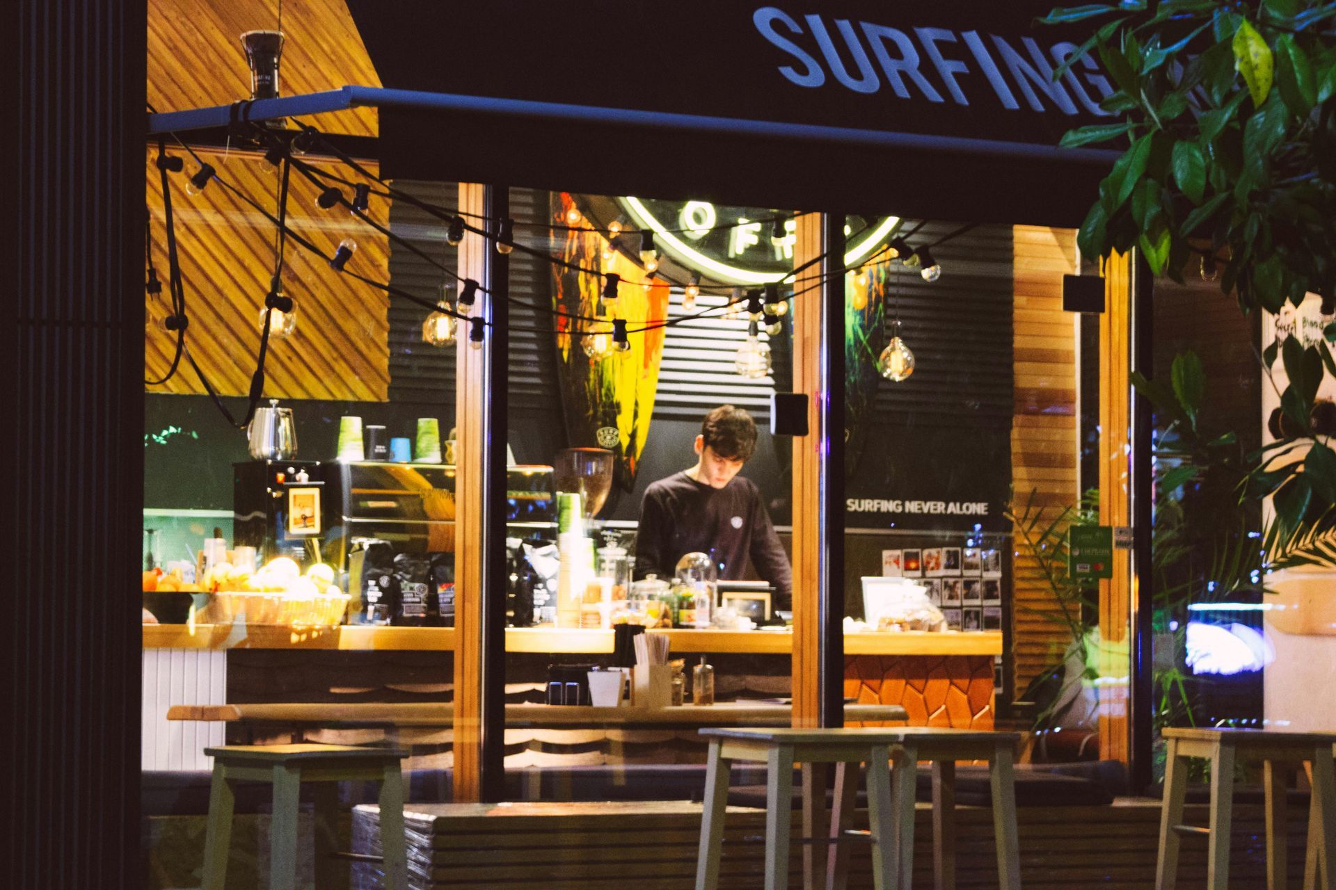 A man is standing in front of a restaurant called surfing.