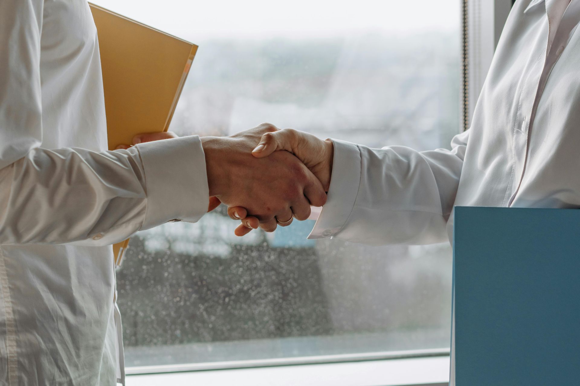 A man and a woman are shaking hands in front of a window.