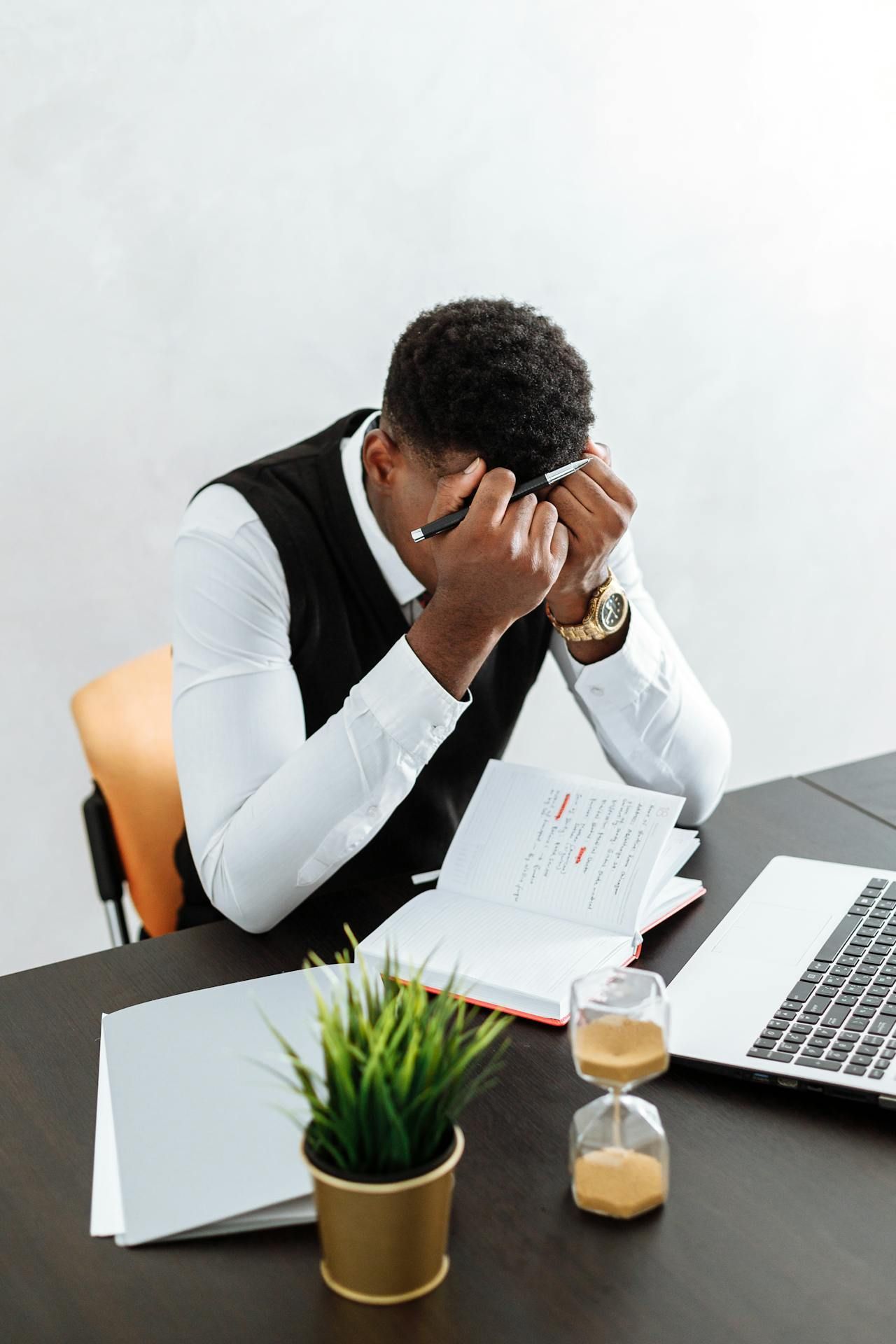A man is sitting at a desk with his head in his hands.