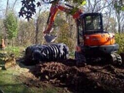 An excavator is digging a hole in the ground in the woods.