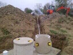 A tractor is digging a hole in the ground next to a pile of dirt.