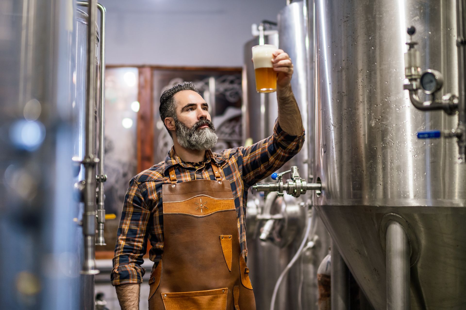 A man is holding a glass of beer in a brewery.