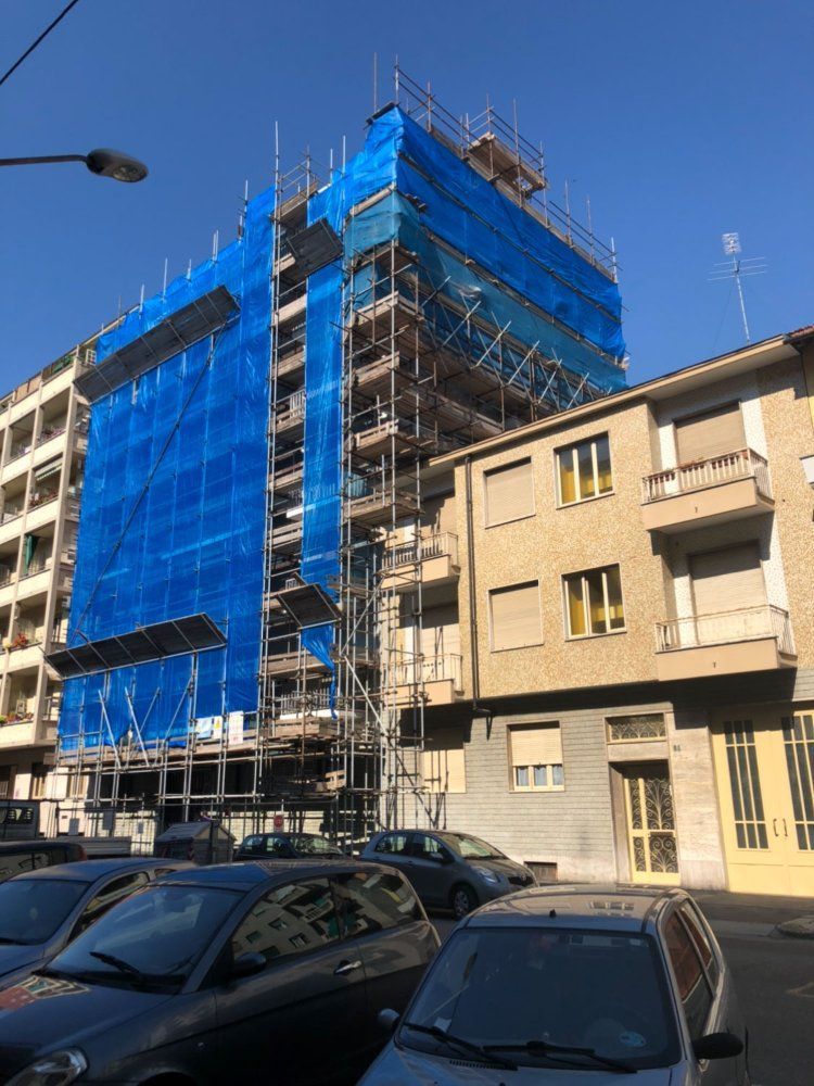 Un edificio in costruzione con impalcature blu e auto parcheggiate davanti.