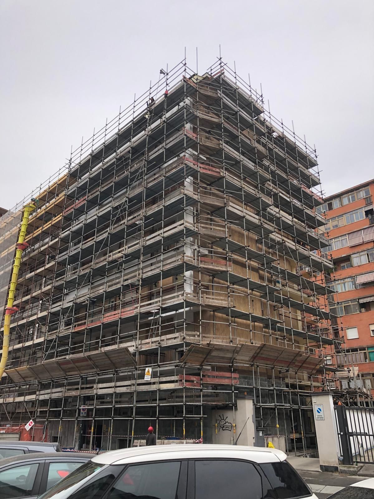 Un edificio in costruzione circondato da impalcature e con un'auto parcheggiata davanti.