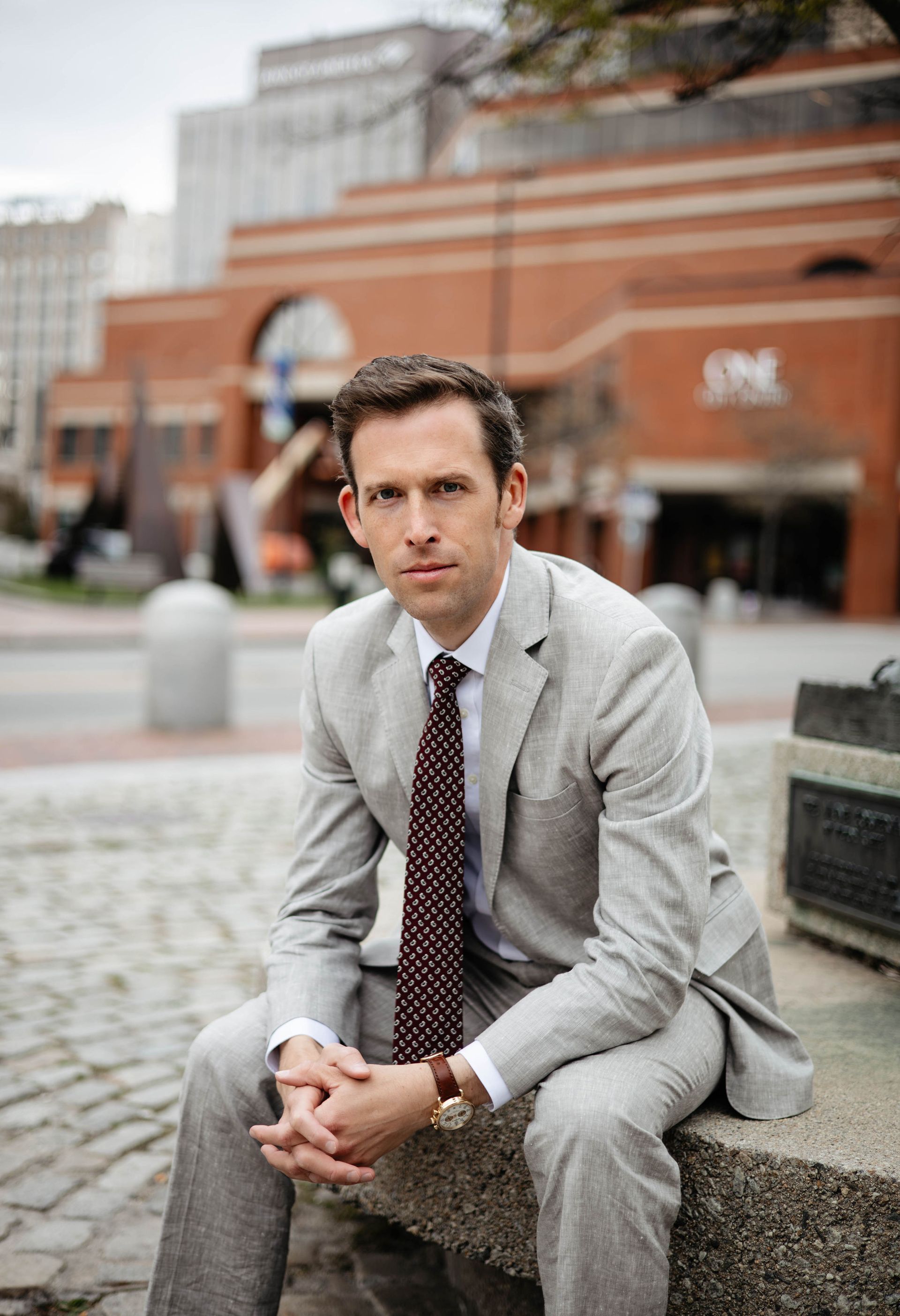 A man in a suit and tie is sitting on a stone ledge.