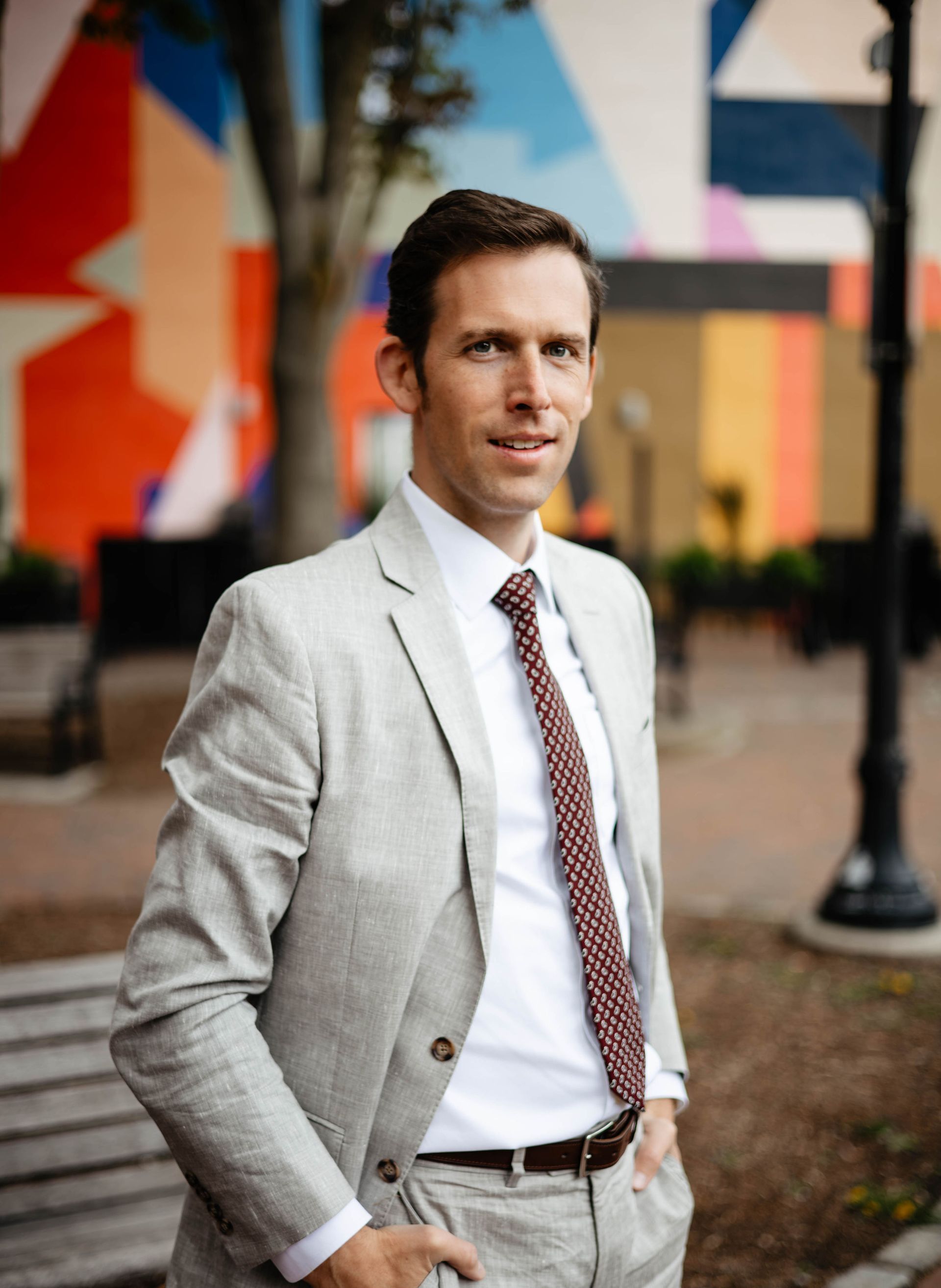 A man in a suit and tie is standing in front of a mural.
