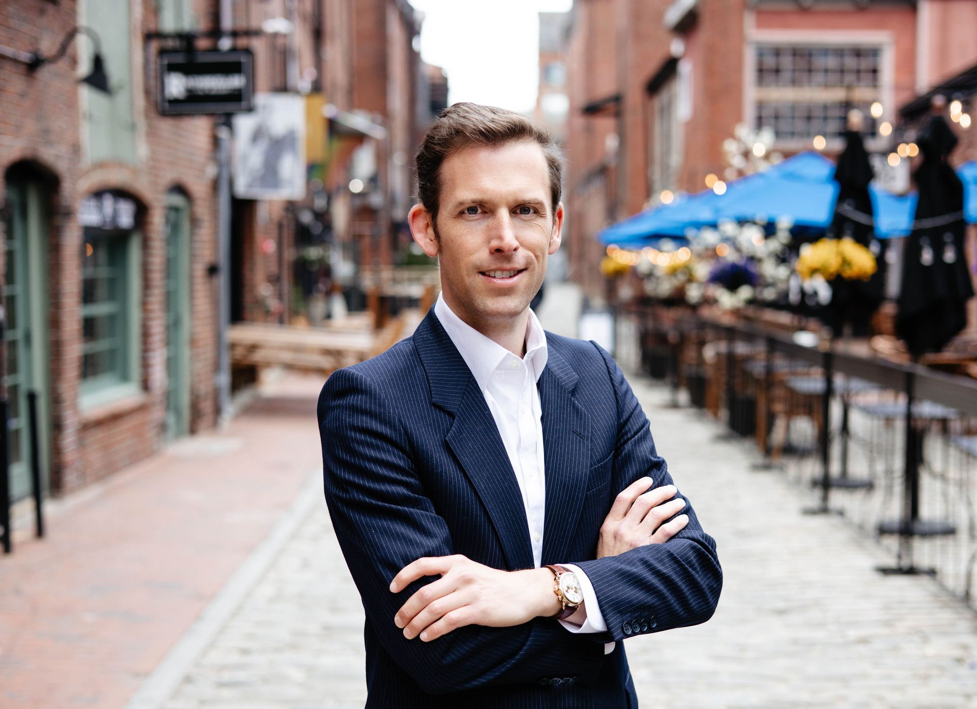 A man in a suit is standing on a cobblestone street with his arms crossed.