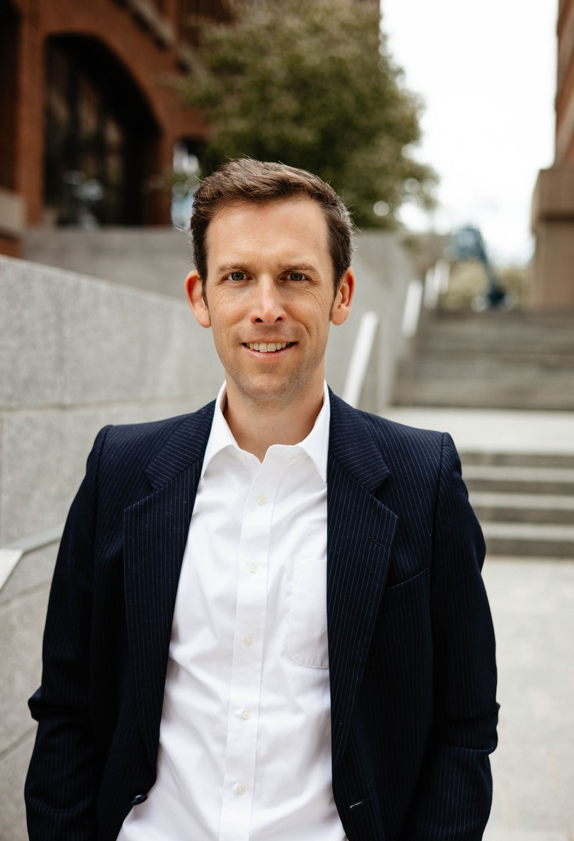 A man in a suit and white shirt is standing in front of stairs.