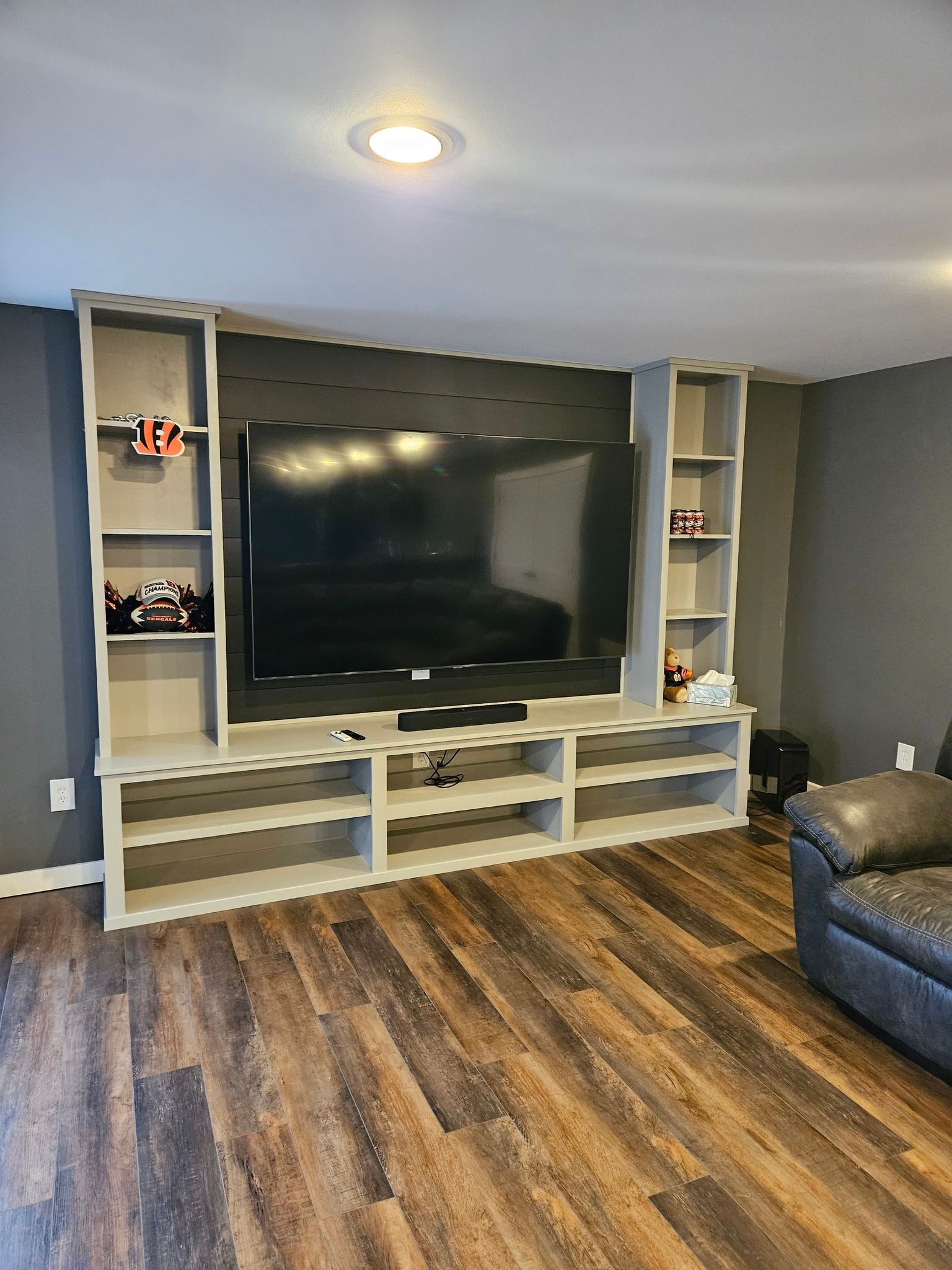 Built-in TV entertainment center with a large screen, shelving, and a dark wood-look floor.